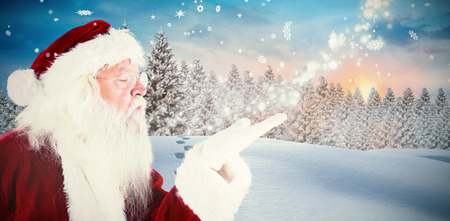 Santa claus blowing against fir tree forest in snowy landscapeの写真素材