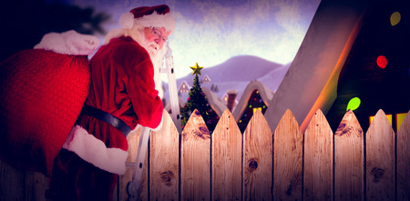Santa steps up a ladder against fence under blue skyの写真素材