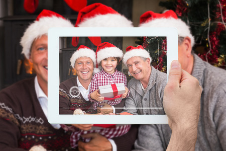 Hand holding tablet pc against three generation family celebrating christmas