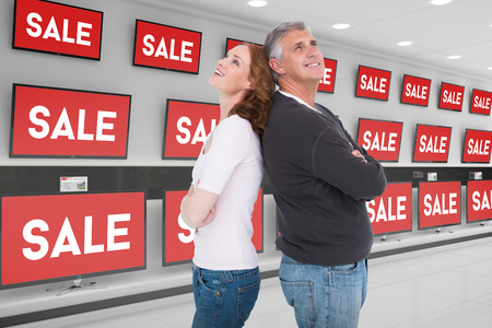 Casual couple smiling and looking up against televisions for saleの写真素材