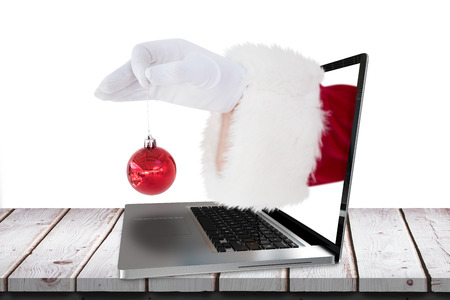 Santa claus holding red bauble against digital image of credit card insert in laptop screenの写真素材
