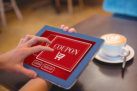 Hand holding digital tablet by table at home against sale advertisementの写真素材