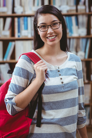 Smiling student with backpack standing in library at the universityの写真素材