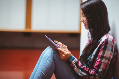 Smiling student sitting on the floor and using tablet at the universityの写真素材