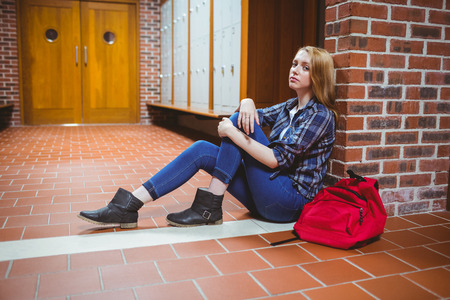 Worried student sitting on the floor against the wall at the universityの写真素材