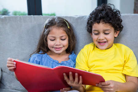 Cute siblings reading a book on the sofa in living roomの写真素材