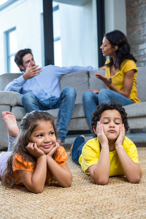 Children laying on the carpet in living room while parents talking on the sofaの写真素材