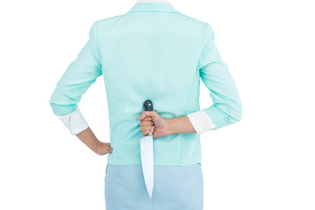 Rear view of businesswoman hiding knife in her back against white backgroundの写真素材