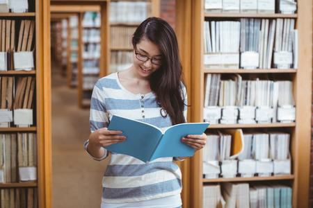 Pretty student reading a book in library at the universityの写真素材