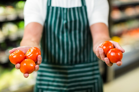 Mid section of worker showing vegetables in supermarketの写真素材