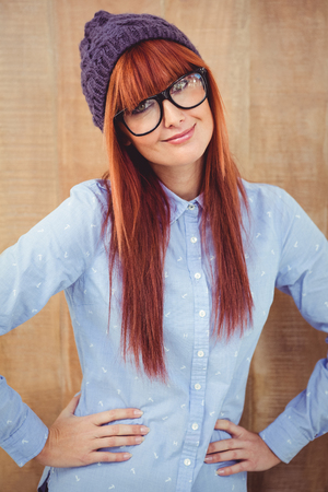 Smiling hipster woman with hands on hips against wooden backgroundの写真素材