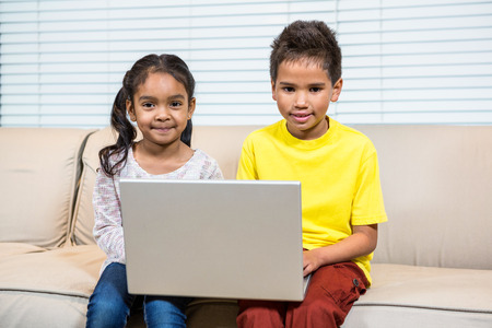 Young smiling siblings using laptop in living room