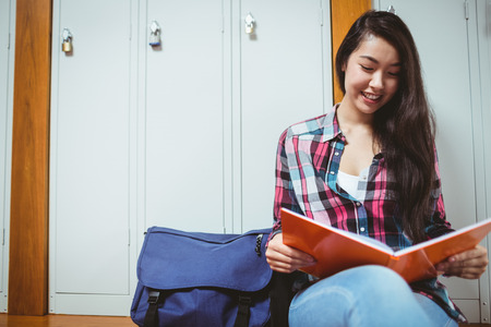 Smiling student sitting and reading a notebook at the universityの写真素材