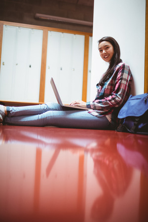 Smiling student sitting on the floor and using laptop at the universityの写真素材