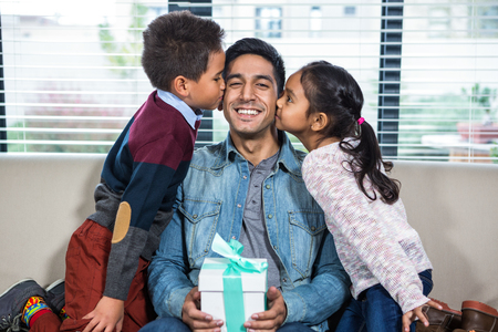 Happy father receiving a gift from his children in living roomの写真素材