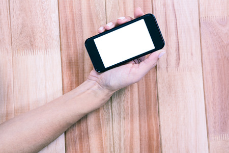Part of hand typing on smartphone on wooden deskの写真素材