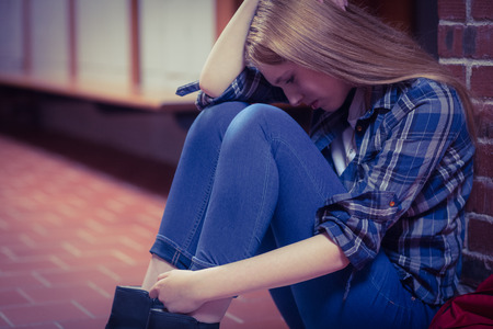 Thoughtful student sitting on the floor against the wall at the universityの写真素材