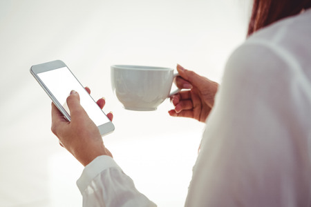 Back view of woman with red hair using smartphone and holding coffee cupの写真素材