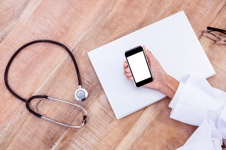 Doctor using smartphone on wooden desk at workの写真素材