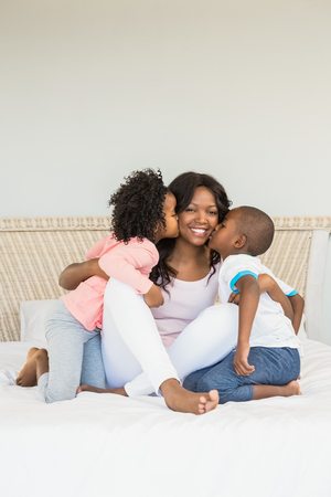 Children kissing mother on bed at homeの写真素材