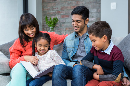 Happy young family reading a book together in living roomの写真素材
