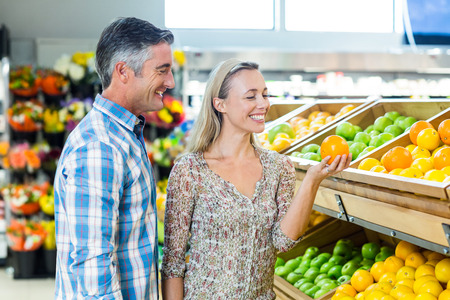 Smiling couple holding an orange in grocery shopの写真素材