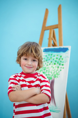 Happy boy with folded arms beside an easelの写真素材