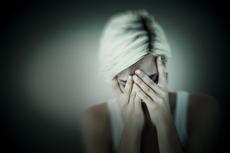 Sad blonde woman crying with head on hands  against grey vignette