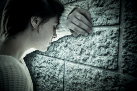 Sad pretty brunette leaning against wall against grey brick wallの写真素材