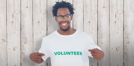 Handsome man pointing to his volunteer tshirt against wooden backgroundの写真素材