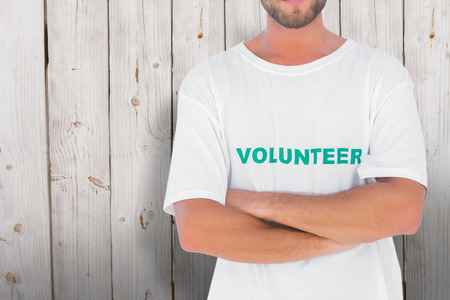 Man wearing volunteer tshirt with arms crossed against wooden backgroundの写真素材