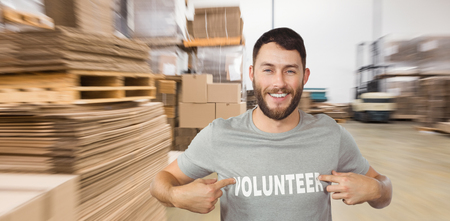 Man showing volunteer text on tshirt  against  cardboard boxes in warehouseの写真素材