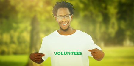 Handsome man pointing to his volunteer tshirt against trees and meadowの写真素材