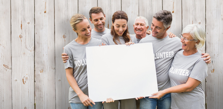 Happy volunteer family holding a blank  against wooden backgroundの写真素材
