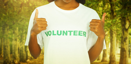 Woman wearing volunteer tshirt and giving thumbs up against walkway along lined trees in the parkの写真素材
