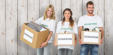 Portrait of three smiling young people with donation boxes against wooden background