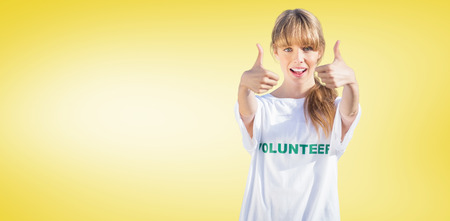 Natural blonde wearing a volunteering t shirt giving thumbs up against yellow vignetteの写真素材