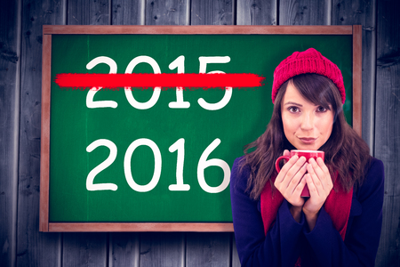 Festive brunette holding a mug against blackboard with copy space on wooden boardの写真素材