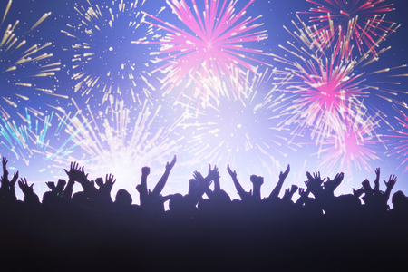 Silhouetters celebrating against colourful fireworks exploding on black backgroundの写真素材