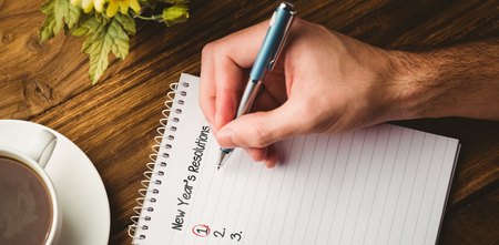 New years resolution list against cropped hand writing in book by coffee cup on tableの写真素材