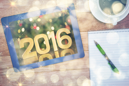 Close-up of golden 2016 against illuminated Christmas tree against view of a blue tablet