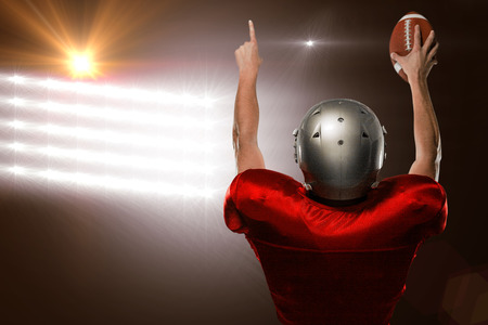 Rear view of American football player with arms raised against spotlights