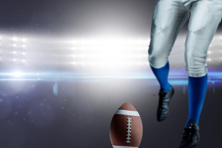Low section of American football player kicking ball against spotlightsの写真素材