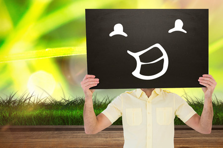 Casual man showing board against wooden planks against dew on grassの写真素材