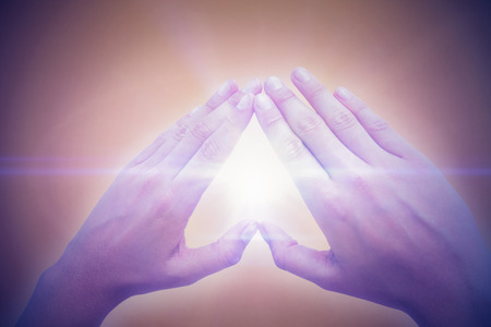 Woman making heart shape with hands against orange backgroundの写真素材