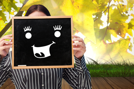 Businesswoman showing board against wooden floor against leavesの写真素材