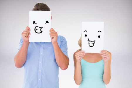 Young couple holding pages over their faces against grey backgroundの写真素材