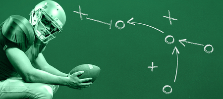 Portrait of American football player crouching while holding ball against greenの写真素材