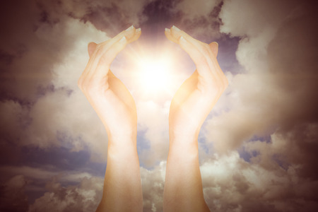 Hands showing against blue sky with white cloudsの写真素材