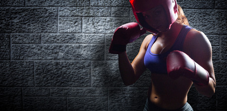 Portrait of female fighter with fighting stance against grey brick wallの写真素材
